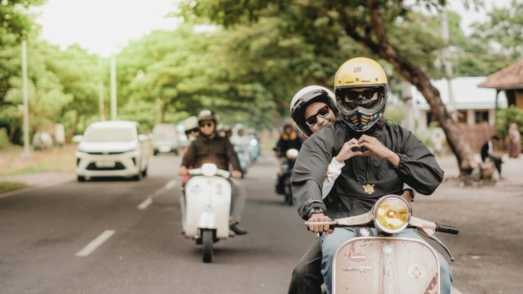 A joyful couple riding a Vespa on a tree-lined street in East Java, Indonesia.