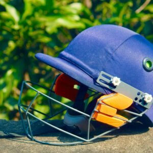 Vibrant blue cricket helmet placed on a stone surface with green foliage background, shot outdoors.