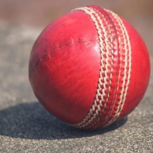 Detailed view of a textured red cricket ball outdoors in sunlight.