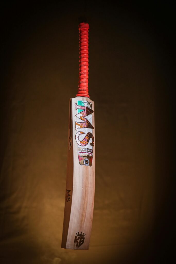 A cricket bat with a red grip, captured against a dark background, emphasizing its sleek design.